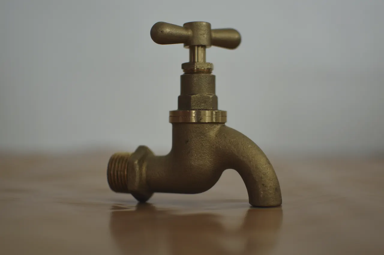 An old brass tap standing on a wooden table in soft light.