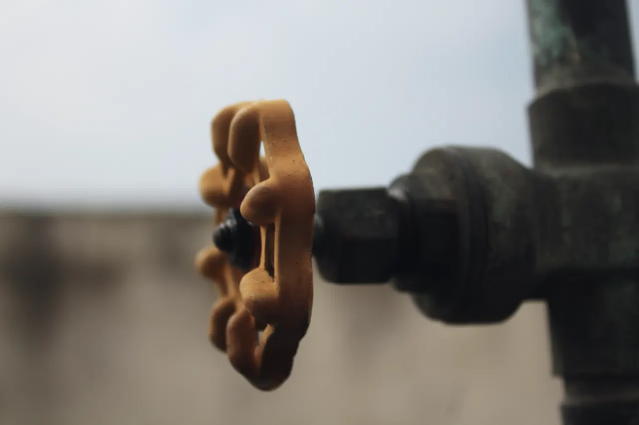 A brass handwheel shut-off valve on an old galvanized pipe, in shallow focus.