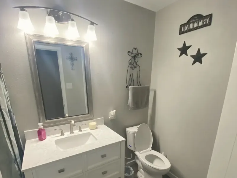 A finished bathroom with a white vanity, a framed mirror, a toilet and gray walls.