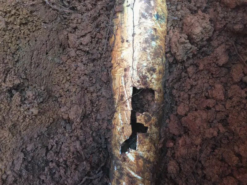 A corroded copper pipe with a hole in it, found in the dirt during a dig.