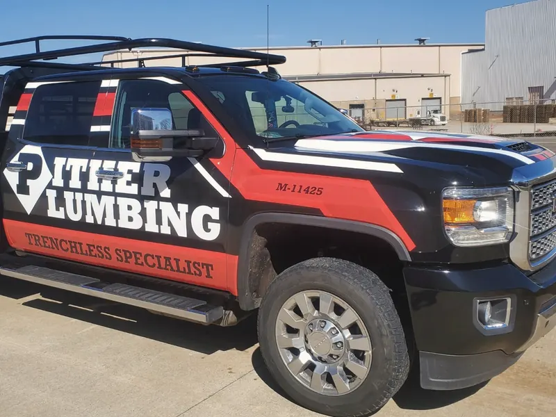 A black and red work pickup with a ladder rack; the door reads Pither Plumbing, Trenchless Specialist, with license M-11425 on the fender.