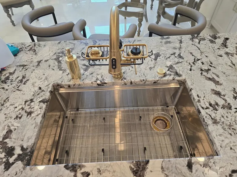 A new stainless workstation sink and a brass faucet set in a granite island.