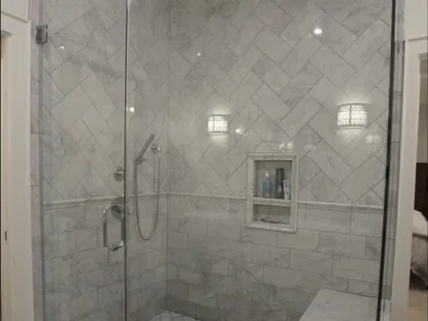 A walk-in shower with a frameless glass door, gray marble tile and a built-in bench.