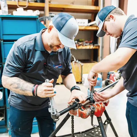 Two technicians threading pipe in the shop, from American Plumbing Co.’s own photographs.